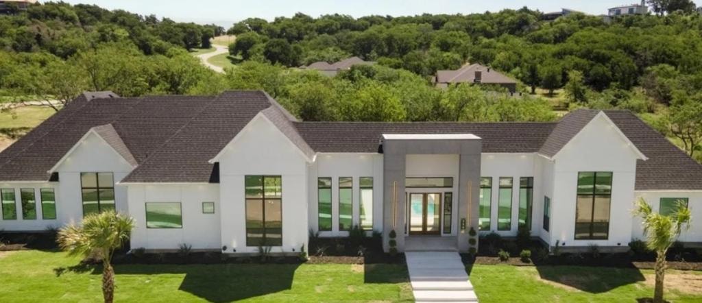 Modern white estate — aerial view with manicured grounds and wooded backdrop