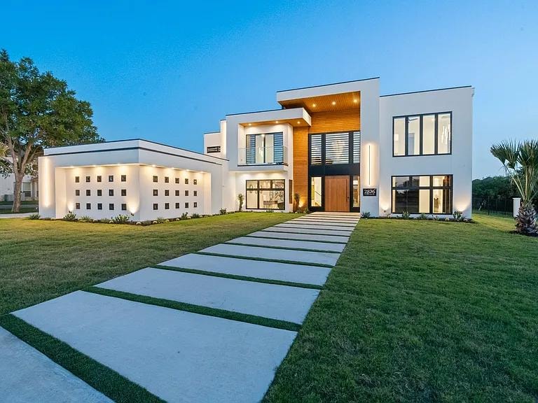 Modern white luxury estate — two-story home with wood accents, stone walkway, and manicured lawn at dusk