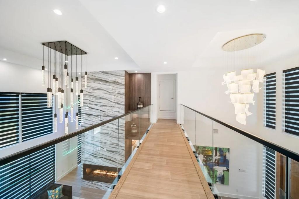 Upper hallway with glass railing, marble accent wall, and cascading crystal chandeliers