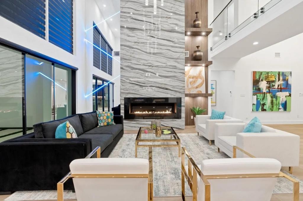 Grand two-story living room with marble fireplace wall, floor-to-ceiling windows, and gold accent furniture