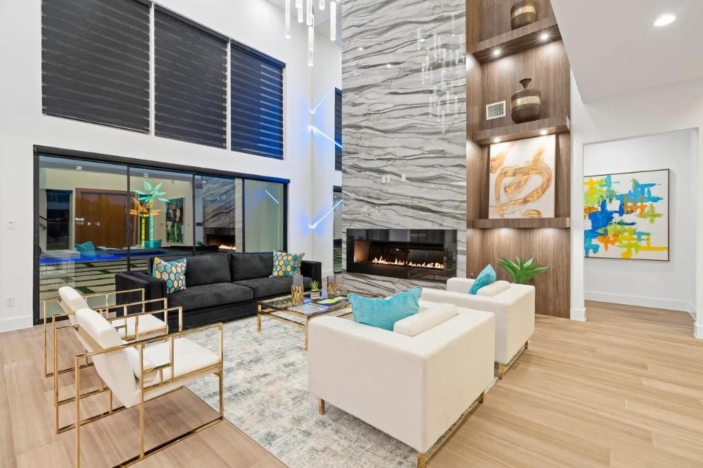 Open-concept living room with soaring ceilings, marble fireplace, and designer gold furnishings