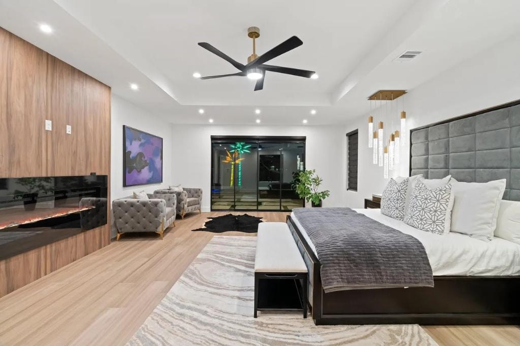 Primary suite with tray ceiling, designer fan, wood accent wall, and pool access